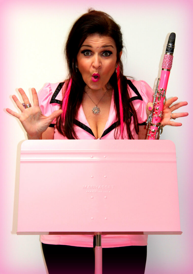 Woman with surprised expression, holding a pink object, behind a pink keyboard, against a pink background.