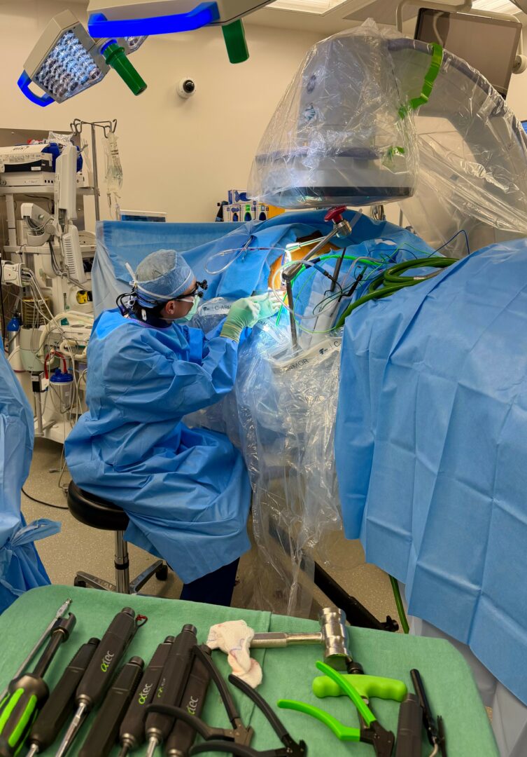 Medical professionals in blue surgical gowns and masks perform a procedure with advanced equipment in an operating room.