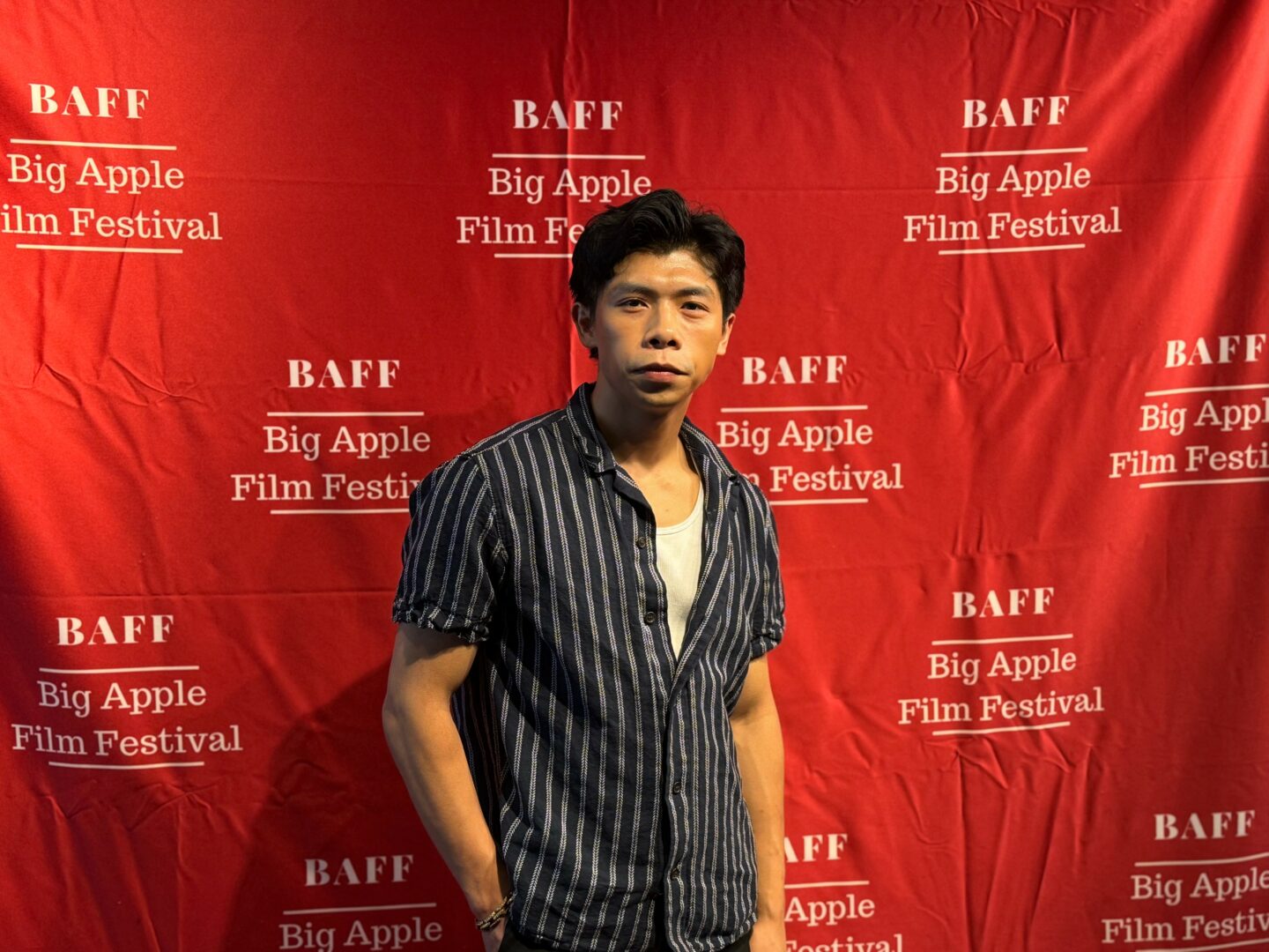 Young man standing in front of a red backdrop with white text for the Big Apple Film Festival.