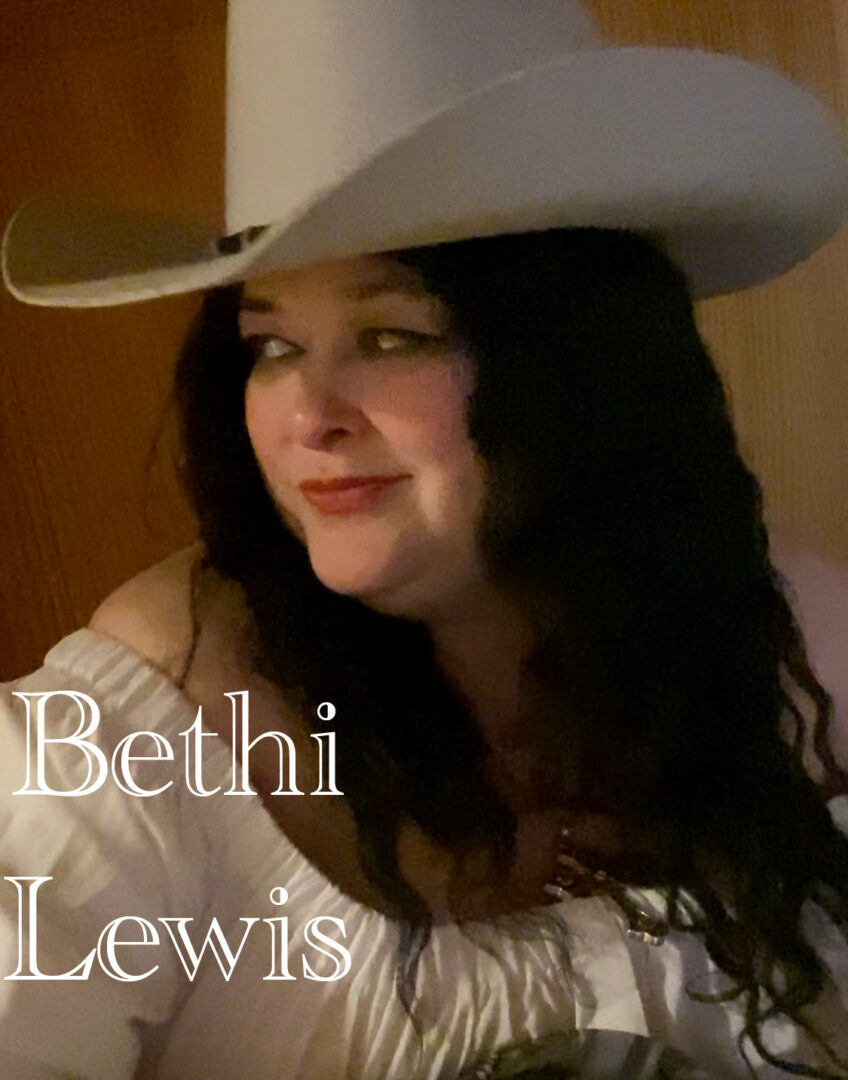 Woman with long dark hair wearing a large white hat and a white top, smiling slightly.