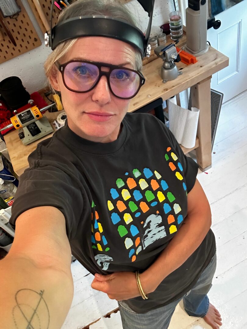 Person wearing glasses and a helmet, taking a selfie in a workshop with tools and equipment in the background.