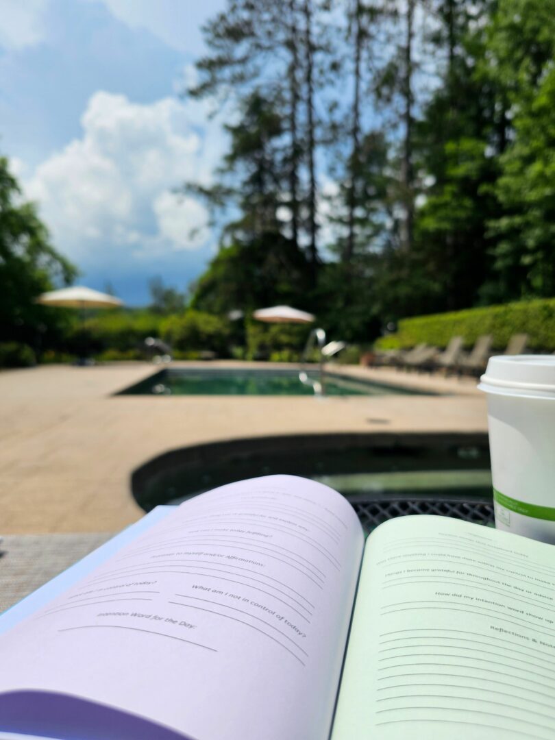 Open book with pages on a table outdoors, trees and sky in background.