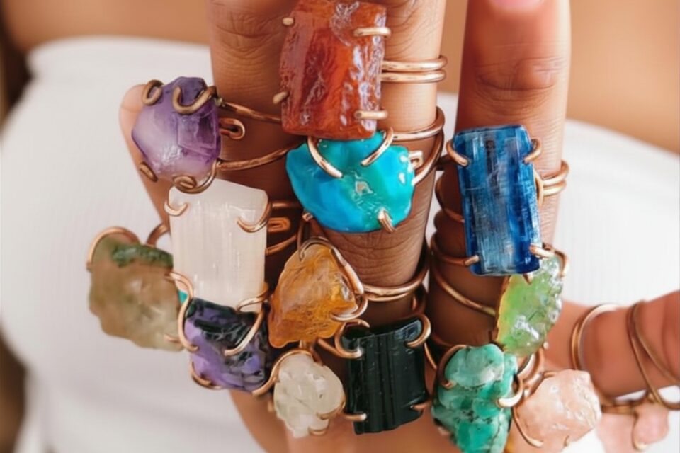 Hand with multiple rings and large colorful gemstone rings on fingers, with a blurred background.