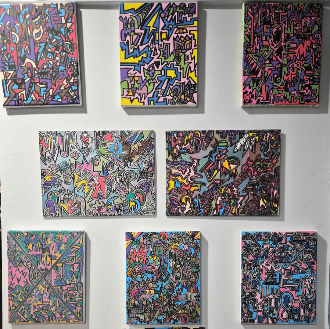 Nine colorful abstract paintings with various geometric and organic shapes arranged in a 3x3 grid on a wall.