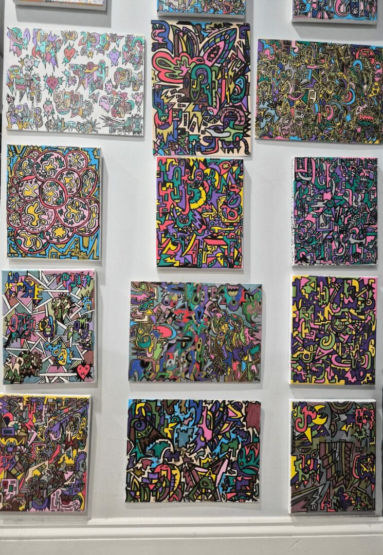 Collection of colorful abstract paintings on a white wall, each with unique intricate patterns and vibrant colors.