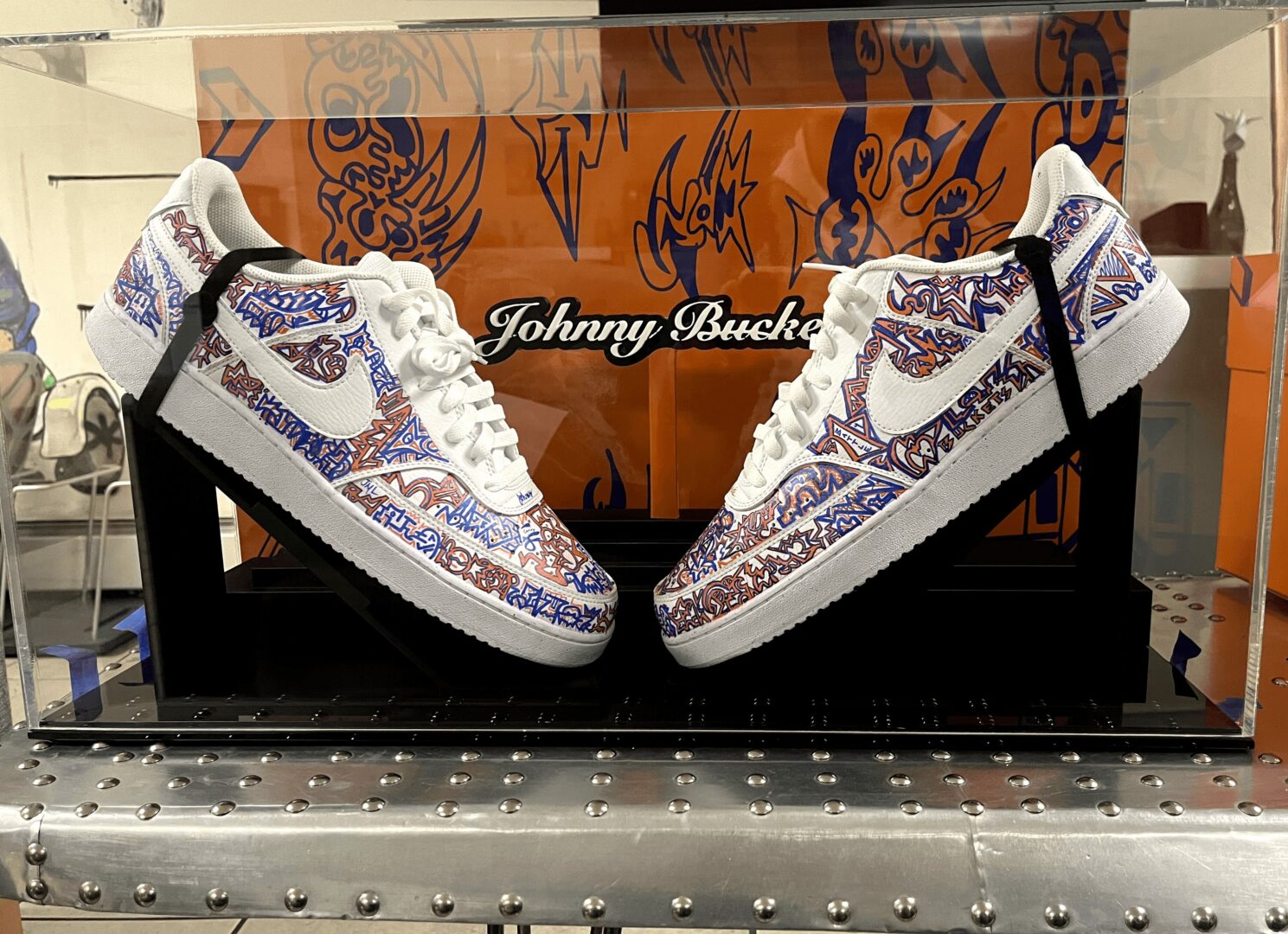 Pair of white sneakers with intricate purple and blue patterns displayed on a black platform.