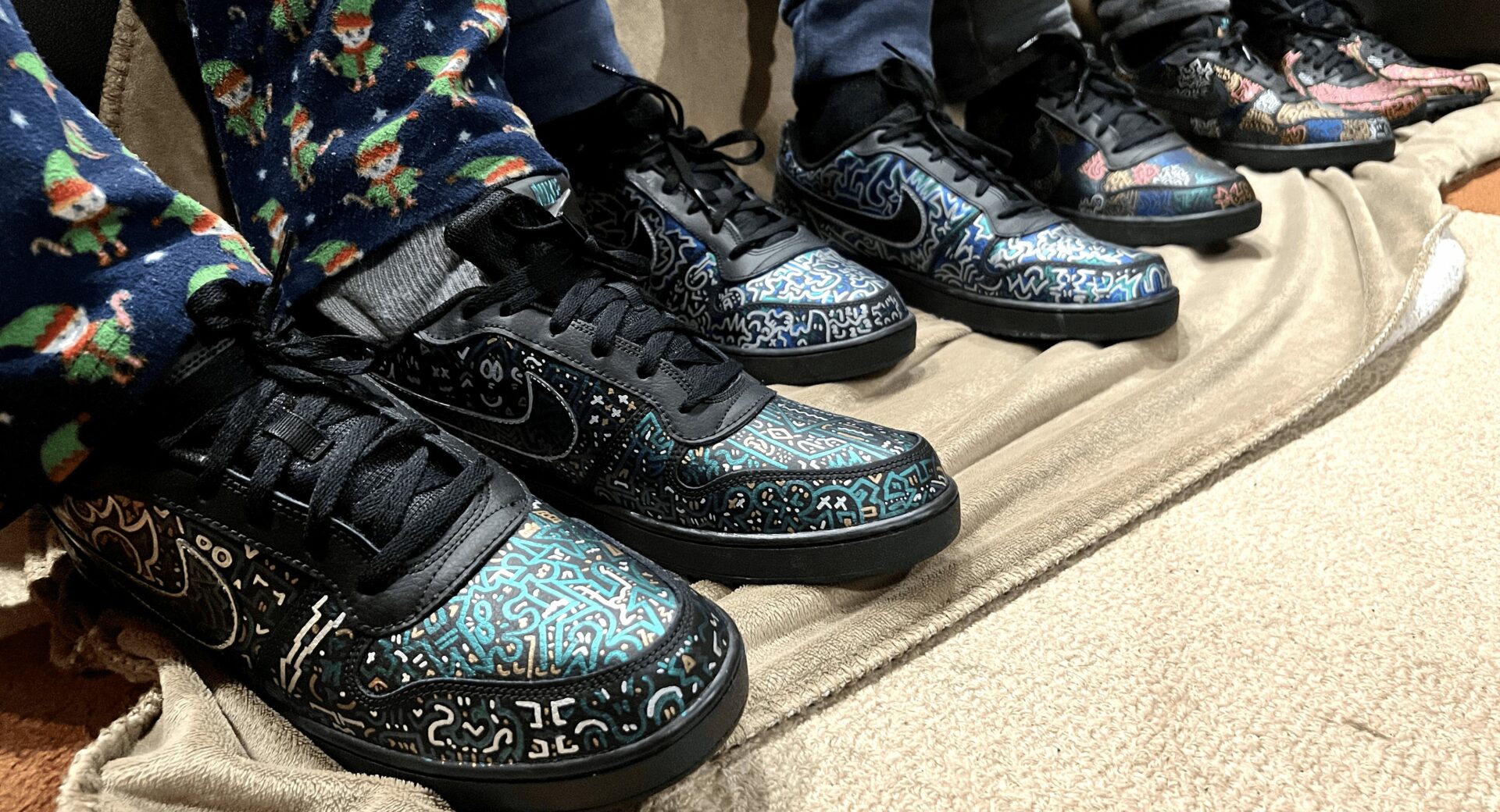 Close-up of five pairs of sneakers on a beige fabric surface, with colorful patterns and black laces.