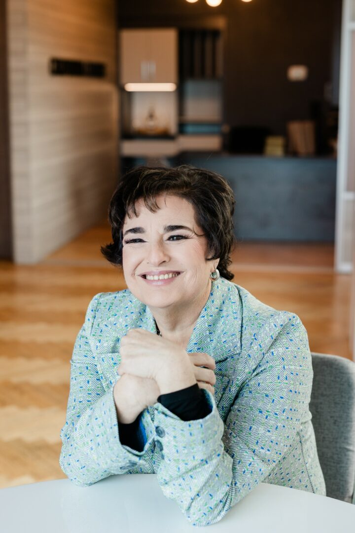 Smiling woman with short dark hair sitting at a table in a modern room.