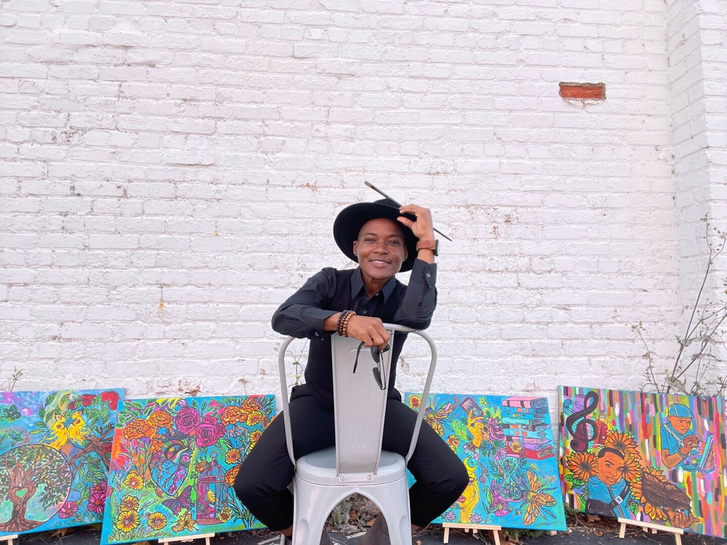 Person sitting on a white scooter in front of colorful artwork on a white brick wall.