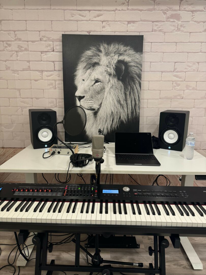 Music production setup with keyboard, speakers, and a lion portrait on brick wall.
