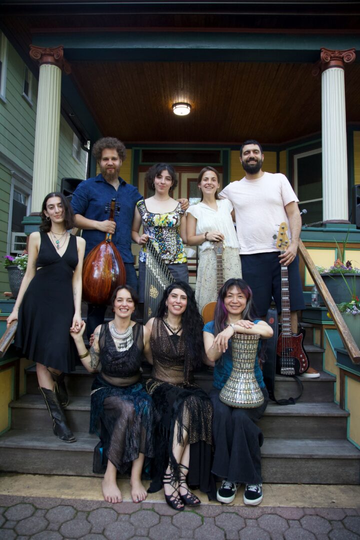 Group of eight people standing and sitting on porch steps outside a house, smiling, with columns and a wooden ceiling.